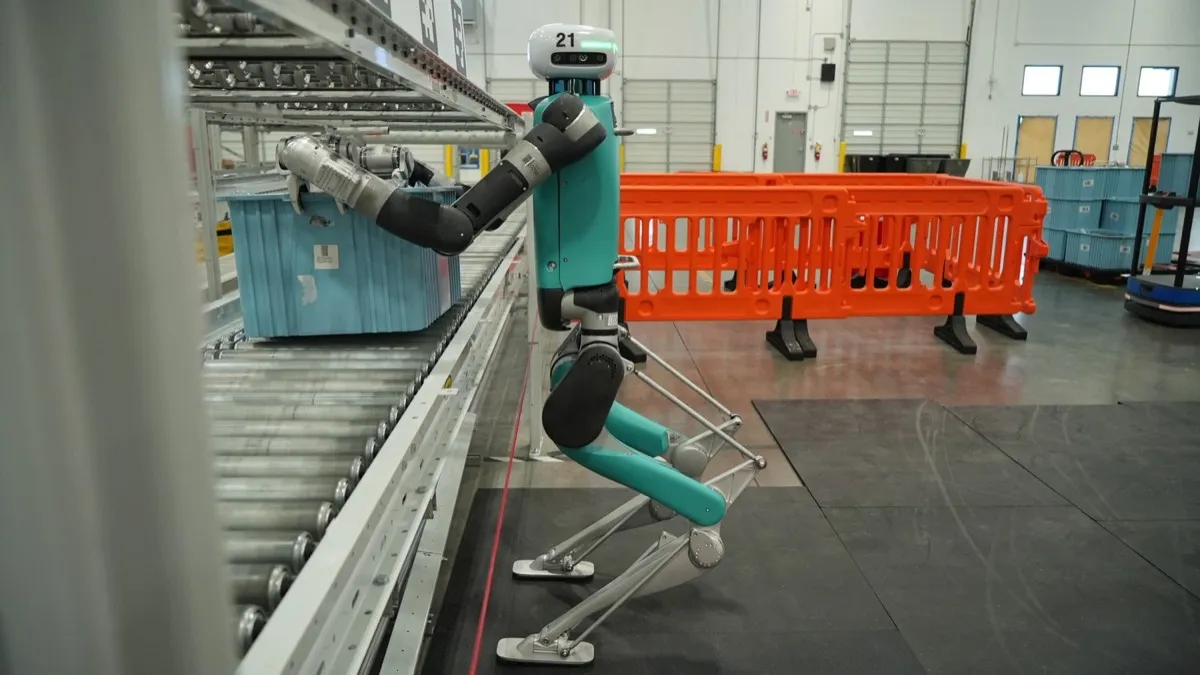 Humanoidní robot Digit od Agility Robotics odkládá plastovou přepravku na válečkový dopravník ve skladu GXO.